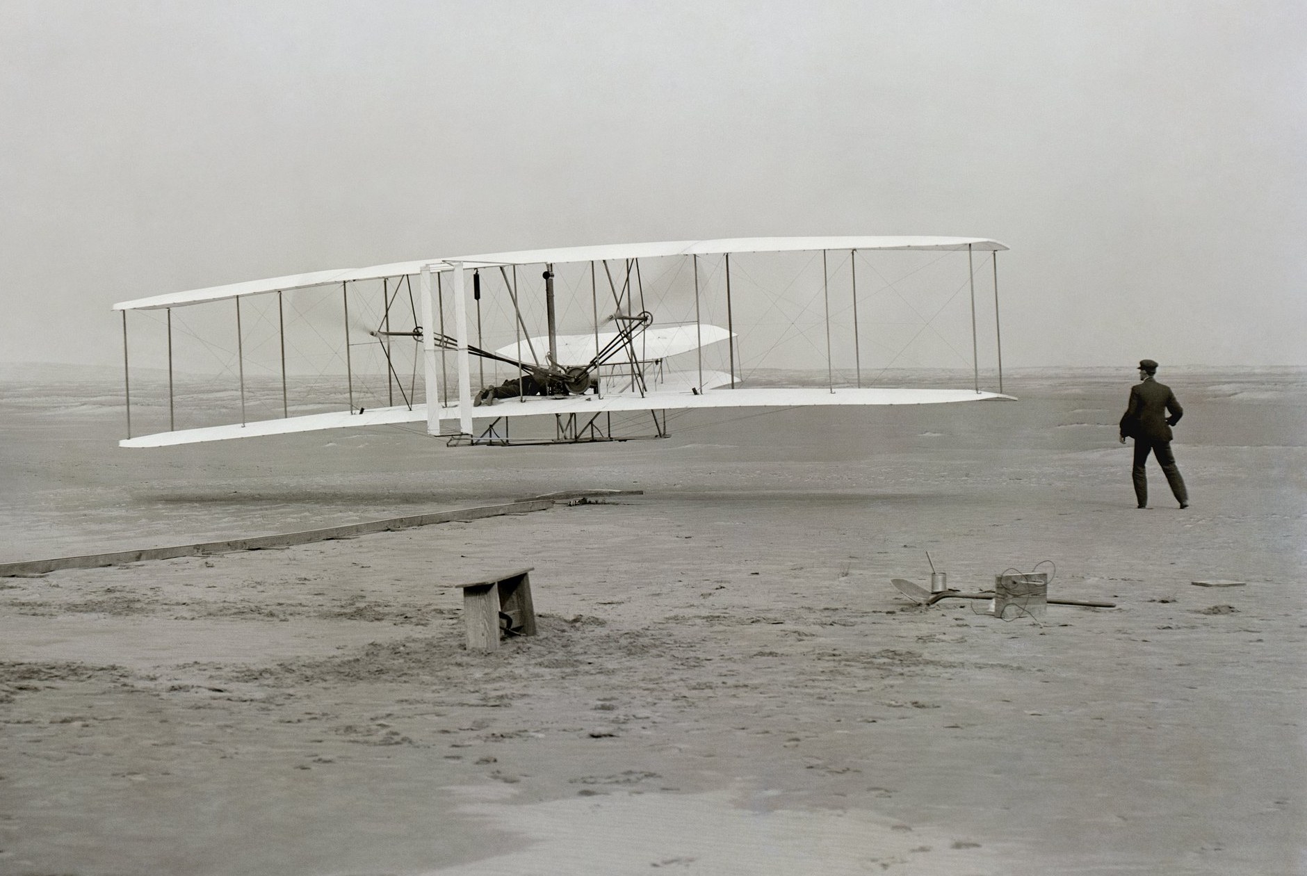 The Wright brothers' first powered flight at Kitty Hawk, December 17, 1903 — the Flyer just off the ground while Wilbur Wright watches from the sand at right